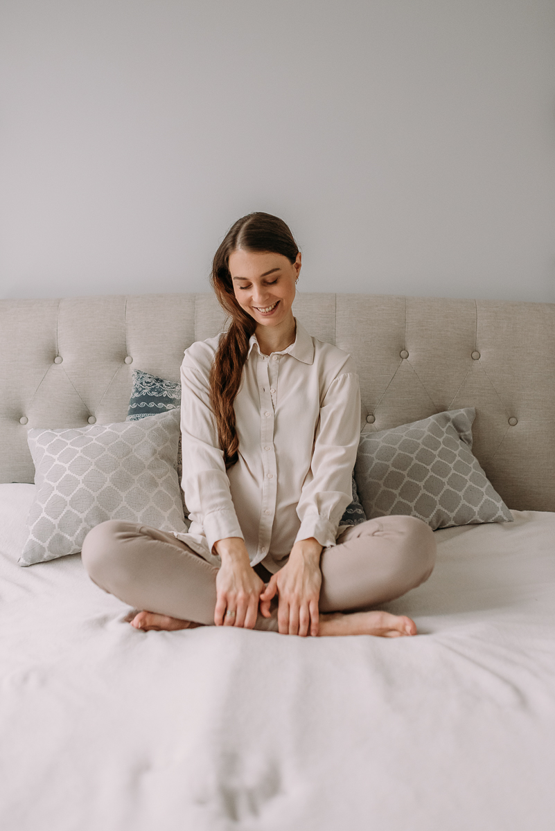 mama w ciąży siedzi na łóżku i pokazuje swój brzuszek