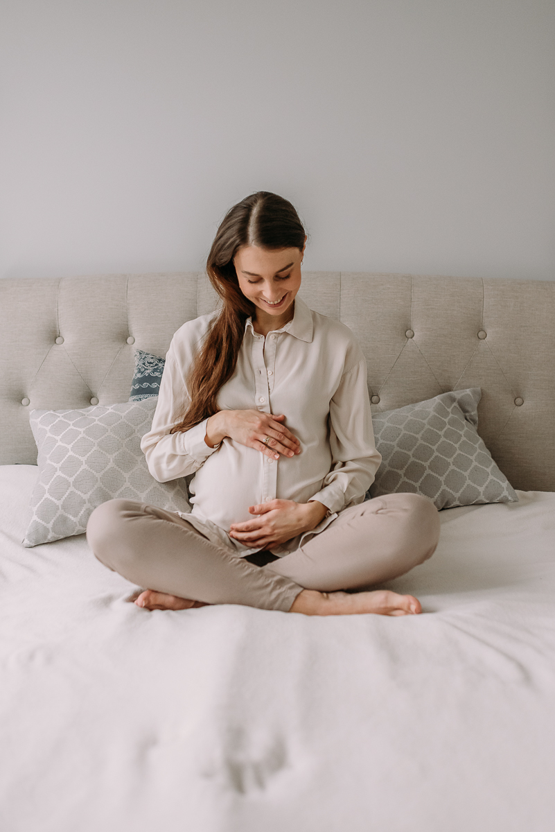 mama w ciąży siedzi na łóżku i głaszcze swój brzuszek