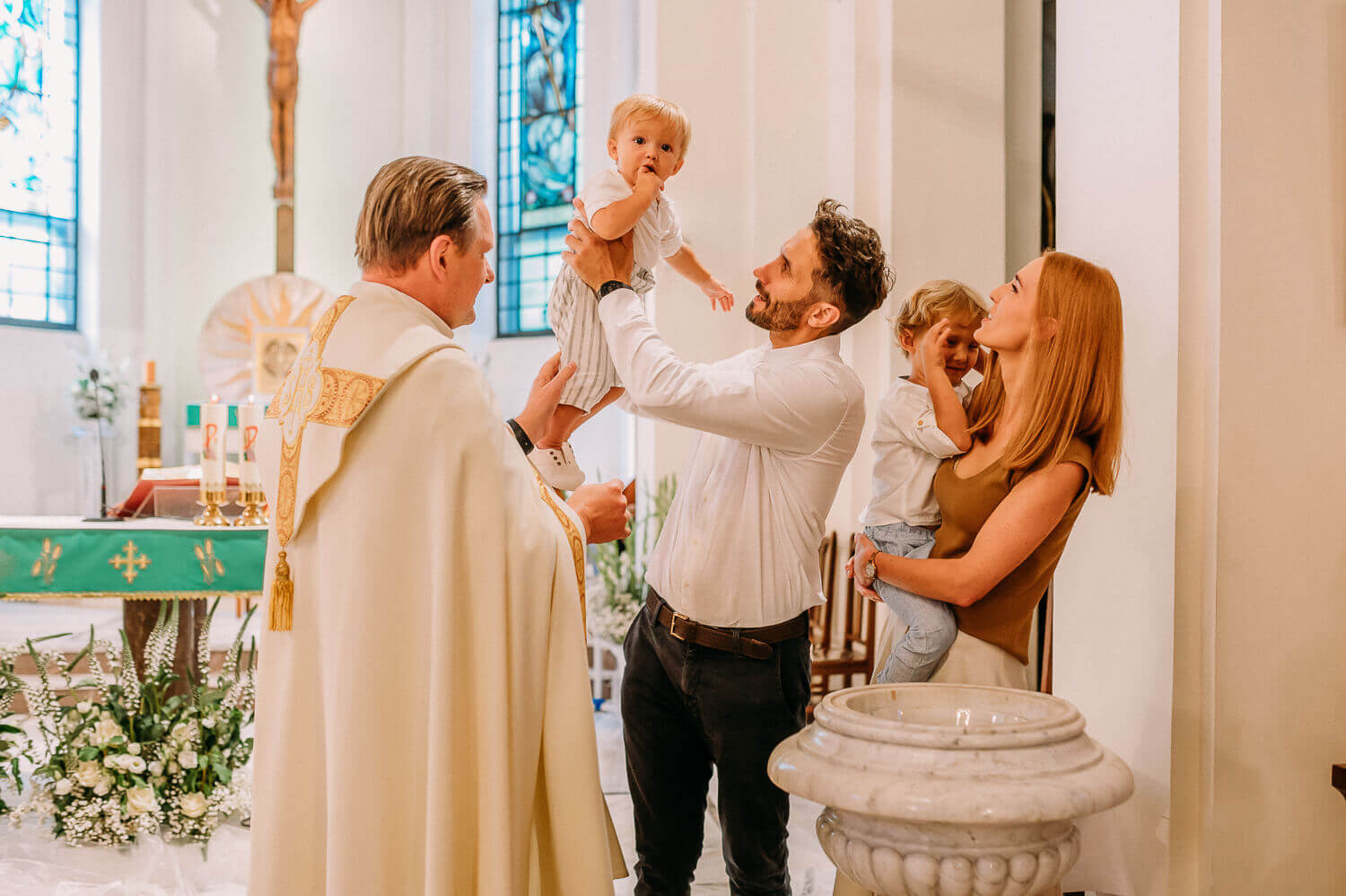 tata podnosi dziecko po chrzcie na tle ołtarza