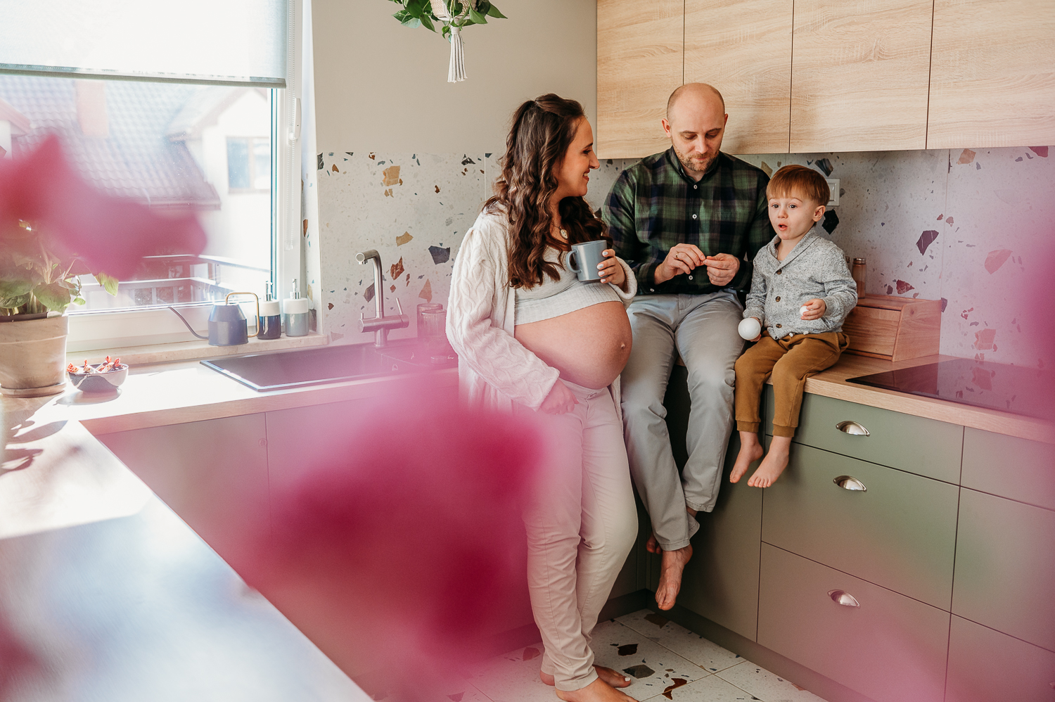 Jak wygląda sesja ciążowa? Najczęstsze pytania przyszłych mam rodzina stoi w kuchni i pozuje do naturalnych zdjęć ciążowych