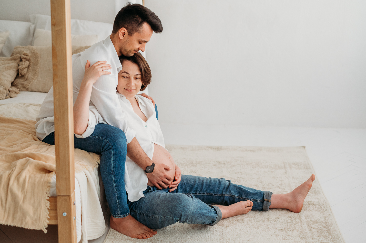 Najczęstsze pytania przyszłych mam - sesja ciążowa w studio, para siedzi na łóżku<br />
