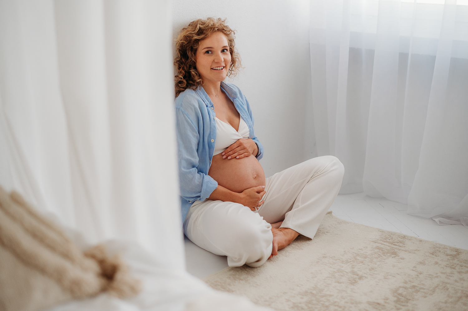 sesja ciążowa w studio - kobieta siedzi i trzyma brzuszek<br />
