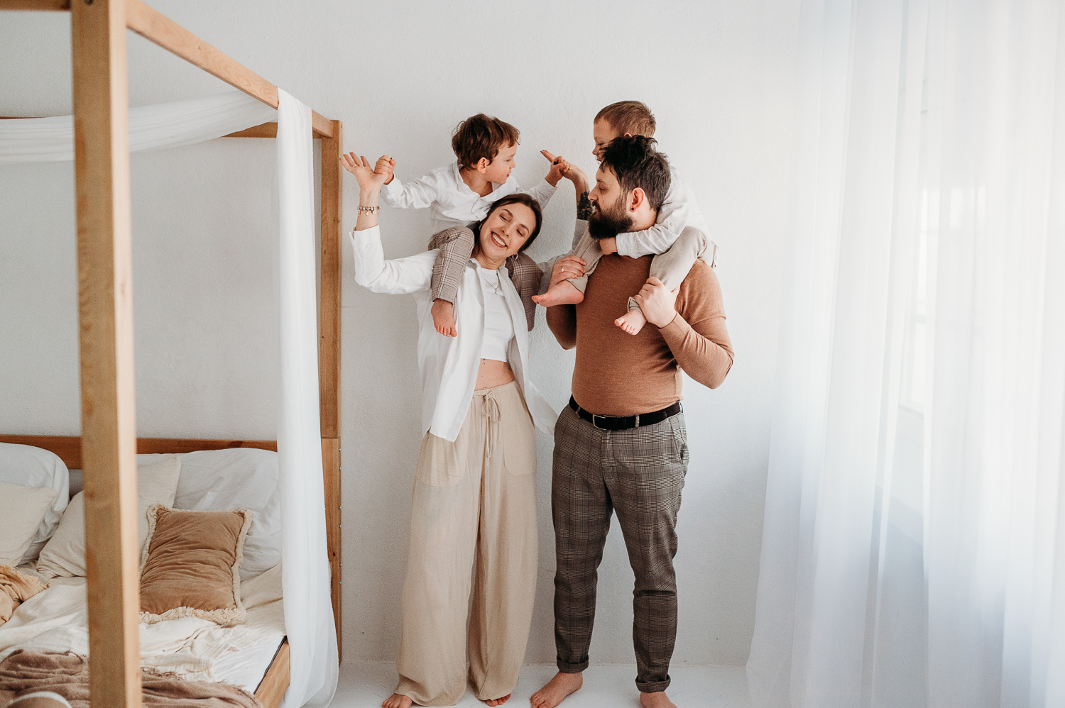 naturalna fotografia rodzinna w studio WArszawa - zdjęcie uśmiechniętej rodzinki, rodzice trzymają dzieci na barana