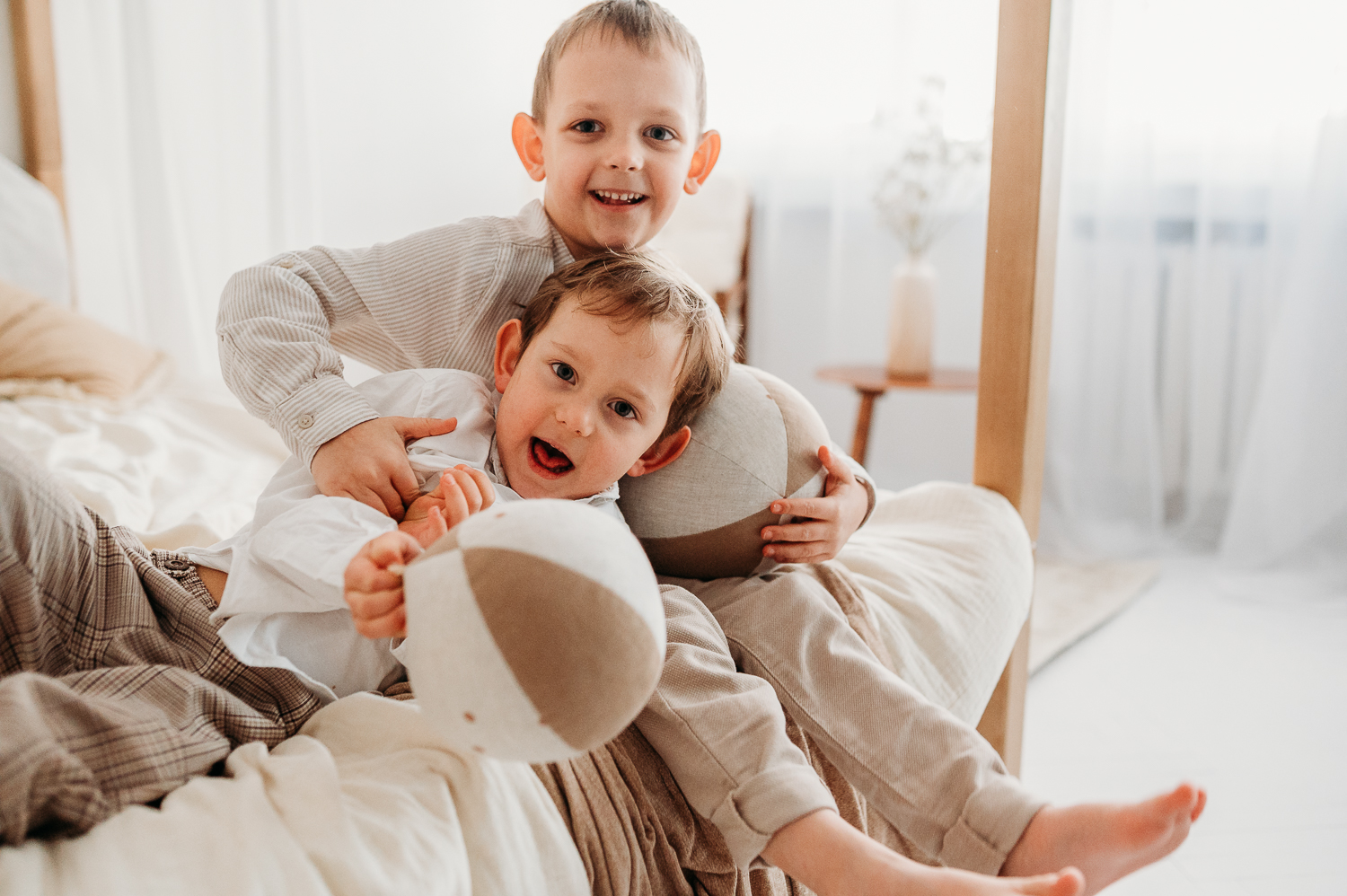 naturalna fotografia rodzinna w studio dwóch chłopców bawi się na łóżku z piłką