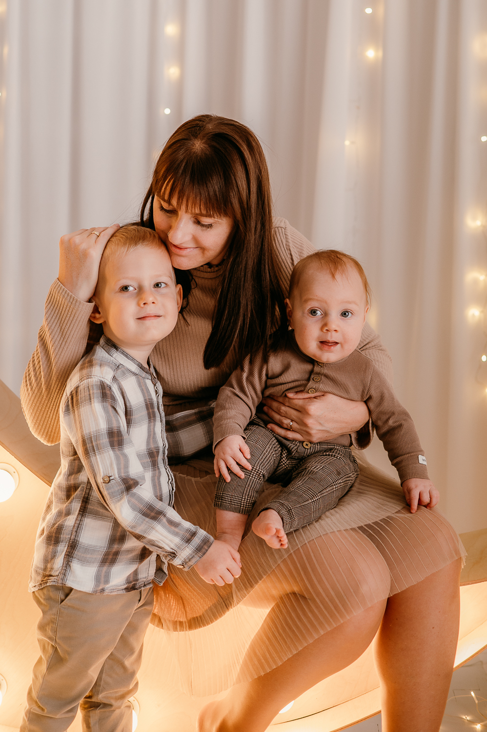 mama siedzi z dwójką dzieci i przytula je podczas świątecznej mini sesji w warszawie