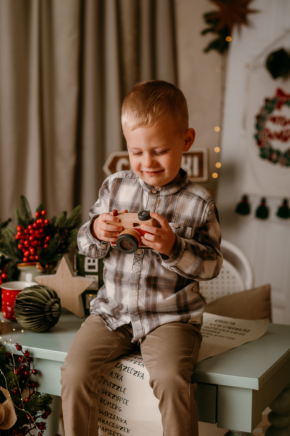 chłopiec siedzi na stole i trzyma zabawkowy aparat i uśmiecha