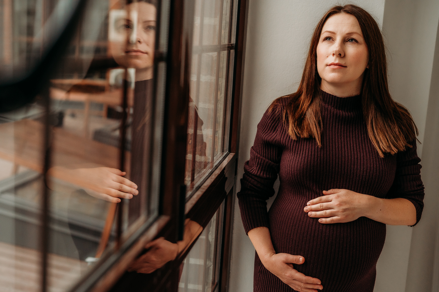 kobieta w ciąży stoi przy oknie i trzyma się na ciążowy brzuszek