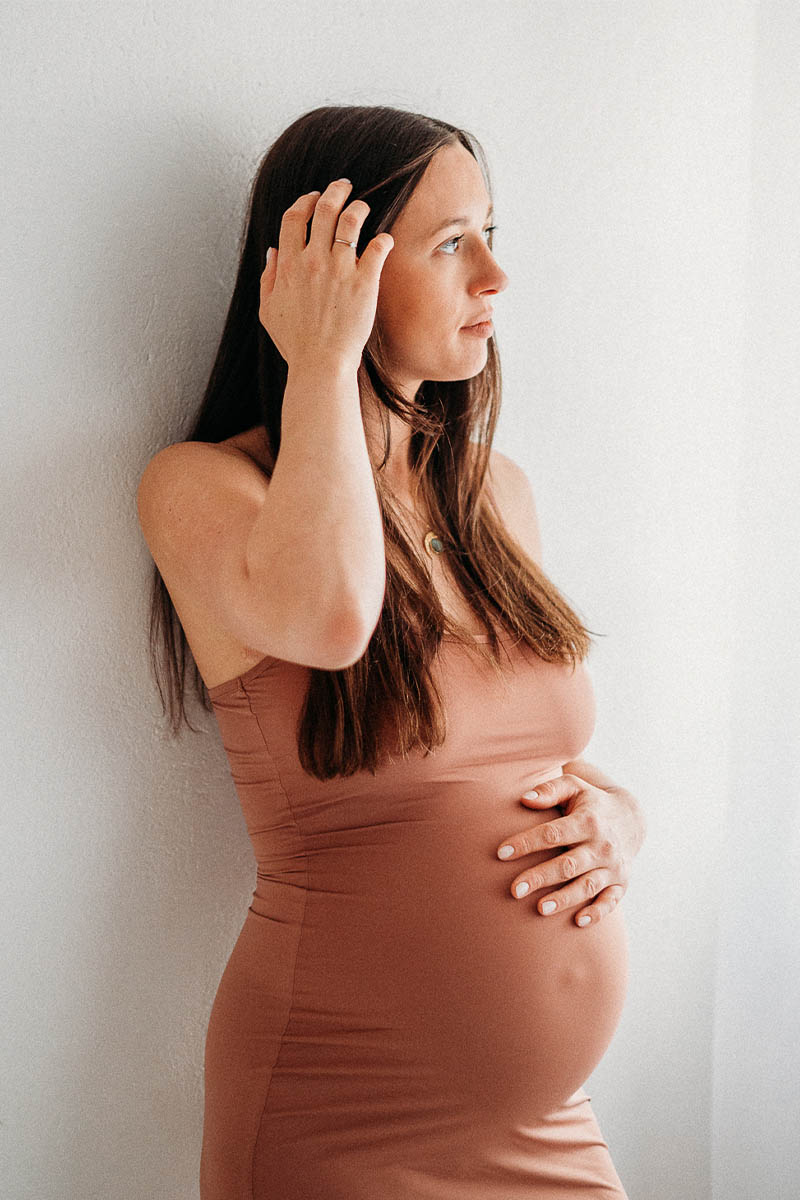 dziewczyna z zaokrąglonym brzuszkiem stoi i pozuje do zdjęć podczas sesji ciążowej