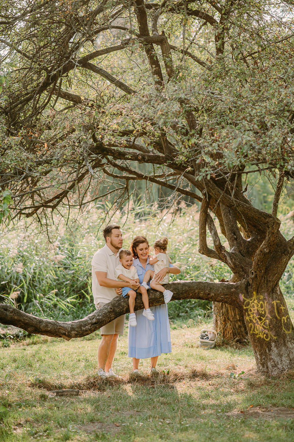 rodzina stoi przy drzewie, bawią się wspinają tak może wyglądać naturalna sesja rodzinna z dziećmi