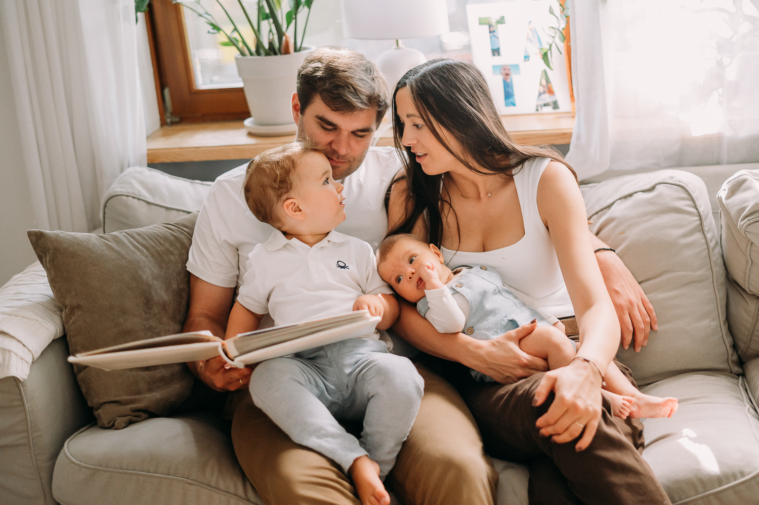 rodzina siedzi na kanapie i czyta wspólnie książkę podczas sesji rodzinnej z małym dzieckiem w warszawie