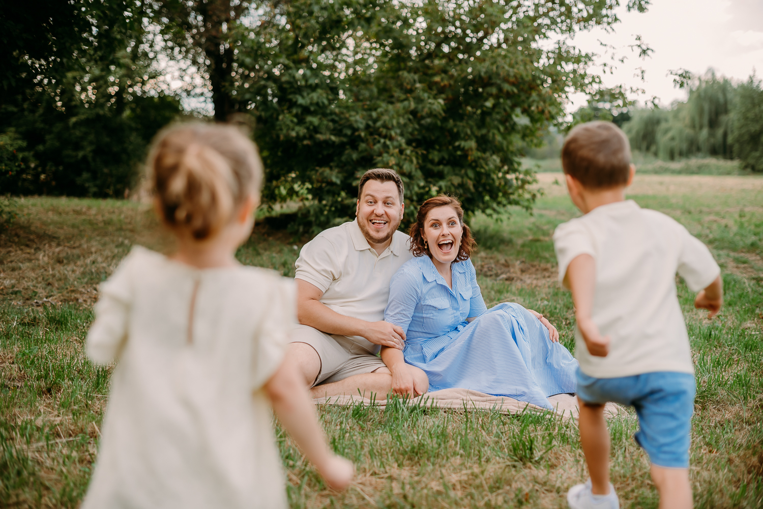 mama z tatą siedzą na trawie, a dwójka dzieci do nich biegnie