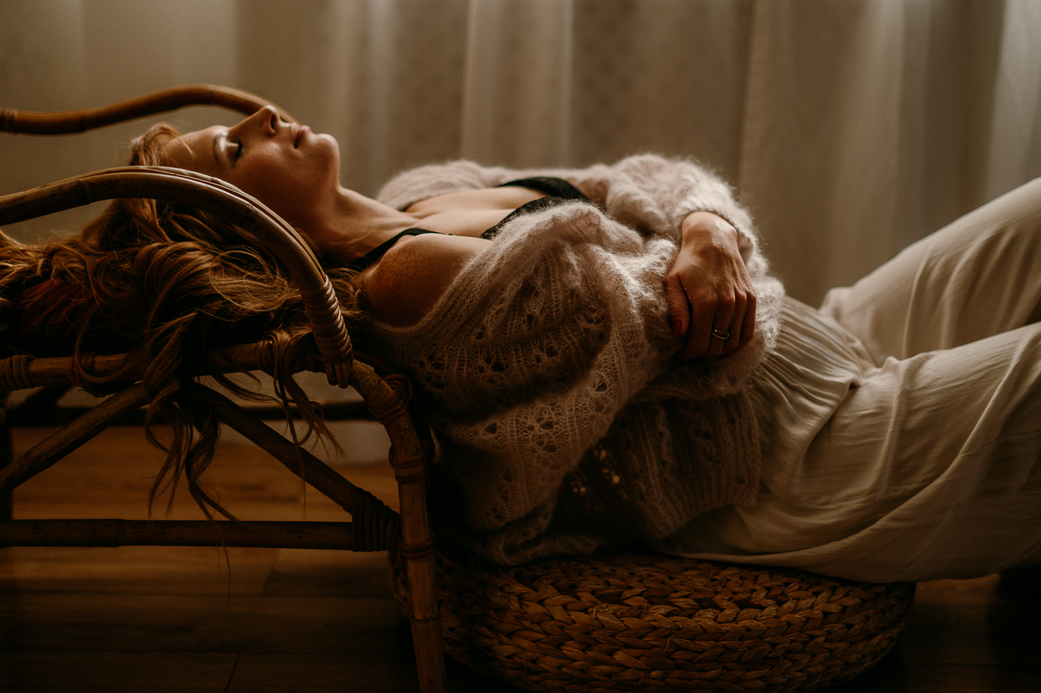 kobieta leży w studio na podłodze i częściowo na wiklinowym fotelu, ma zamknięte oczy i czule głaszcze się po klatce piersiowej<br />
